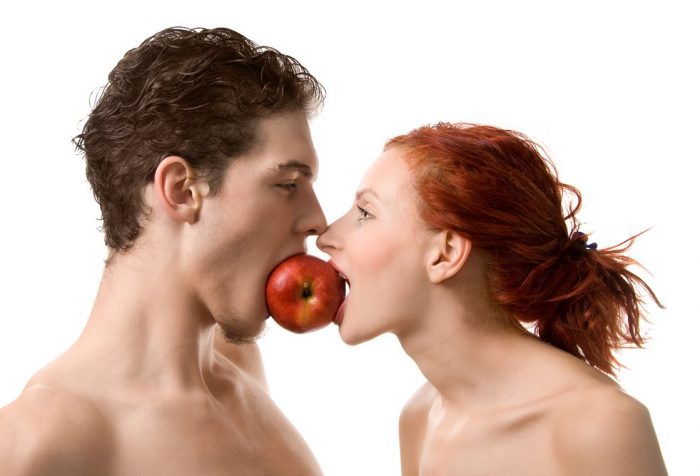 Обнаженные мужчина и женщина кусают одно яблоко